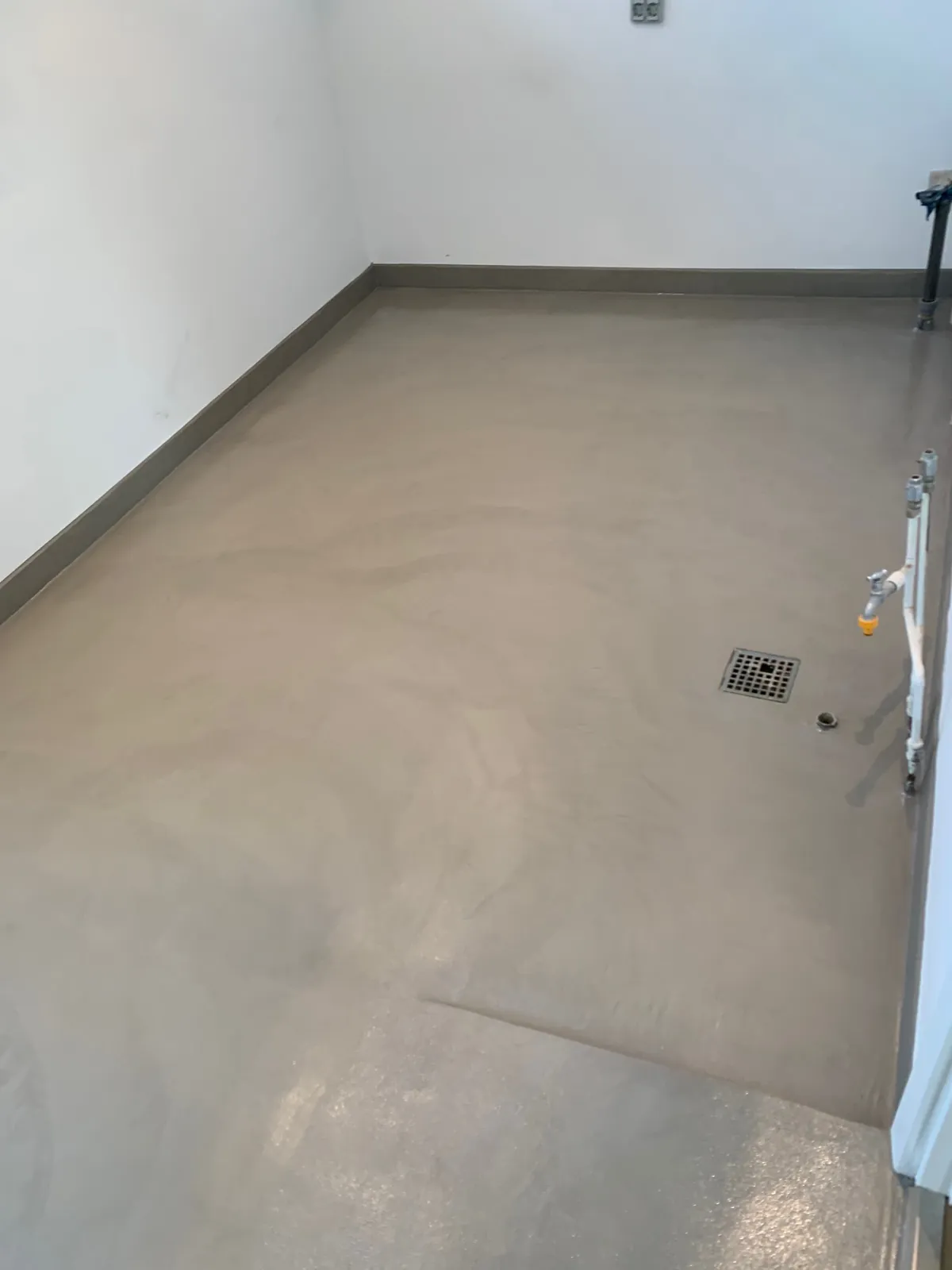 Lysegråt microcementgulv i tomt rum med afløb – Maler Microcement, Herlev og omegn